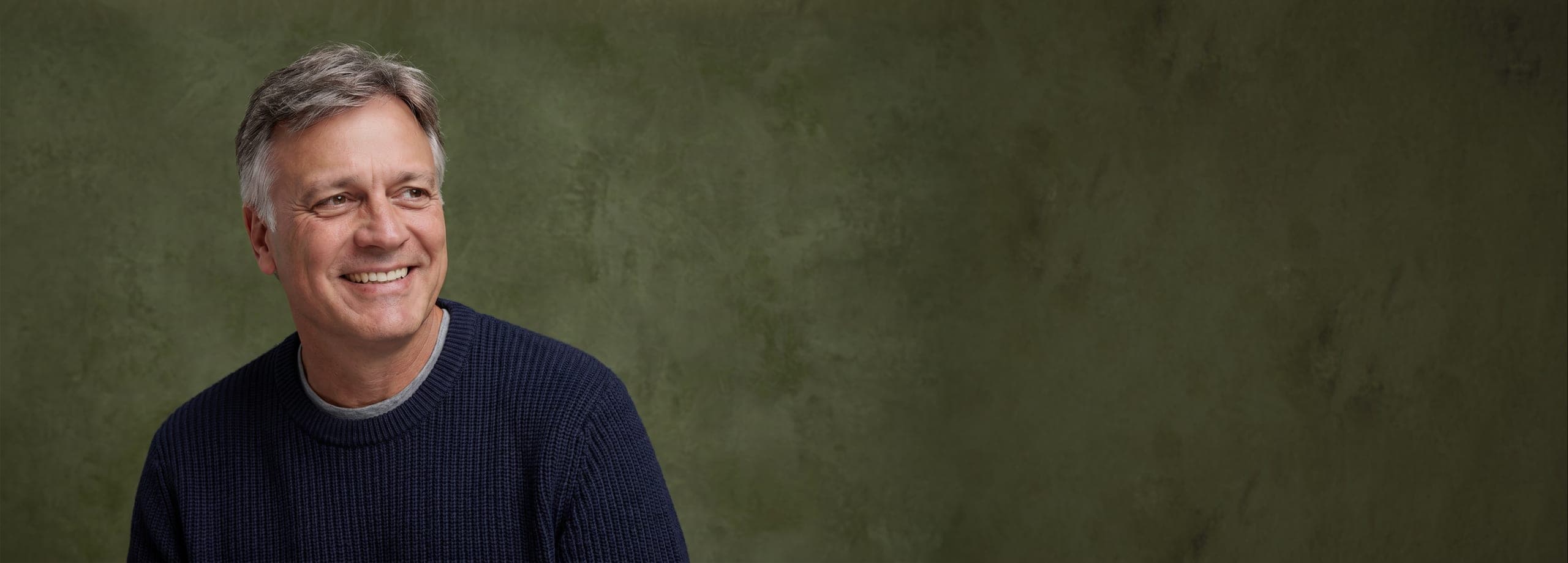 Michael Scarano seated, lit warmly against a dark green backdrop