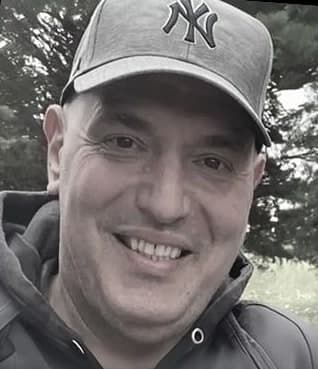 Fotis Manouvelos smiling outdoors, wearing a New York Yankees cap
