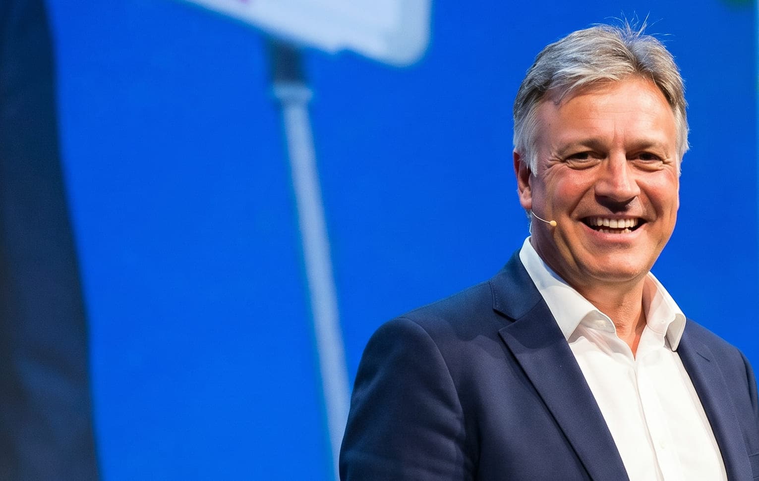 Michael Scarano speaking on stage, smiling, against a blue backdrop