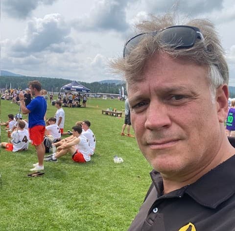 Michael Scarano at a youth sports event, fields and teams behind him