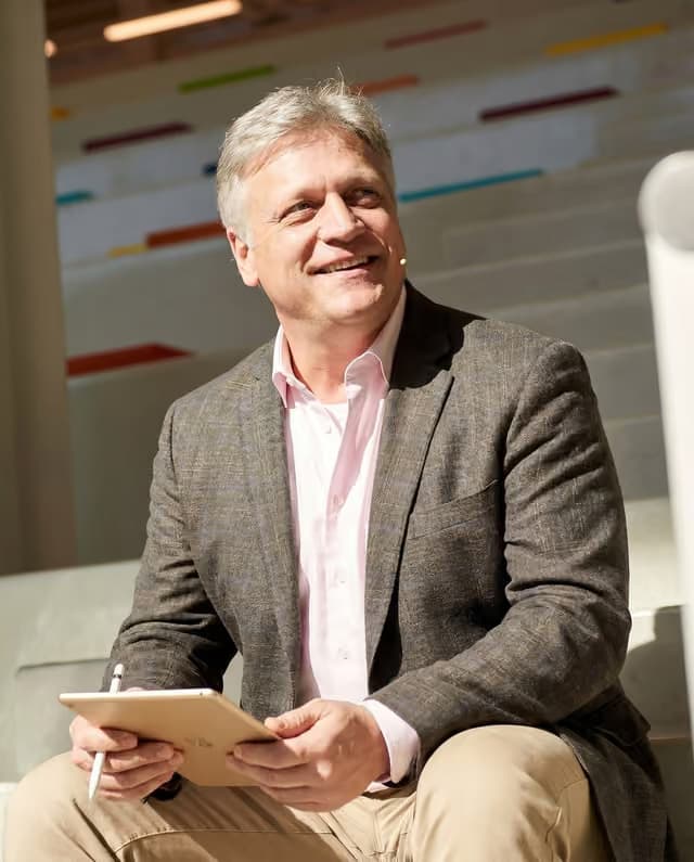 Michael Scarano seated with a tablet, wearing a headset microphone, smiling off camera