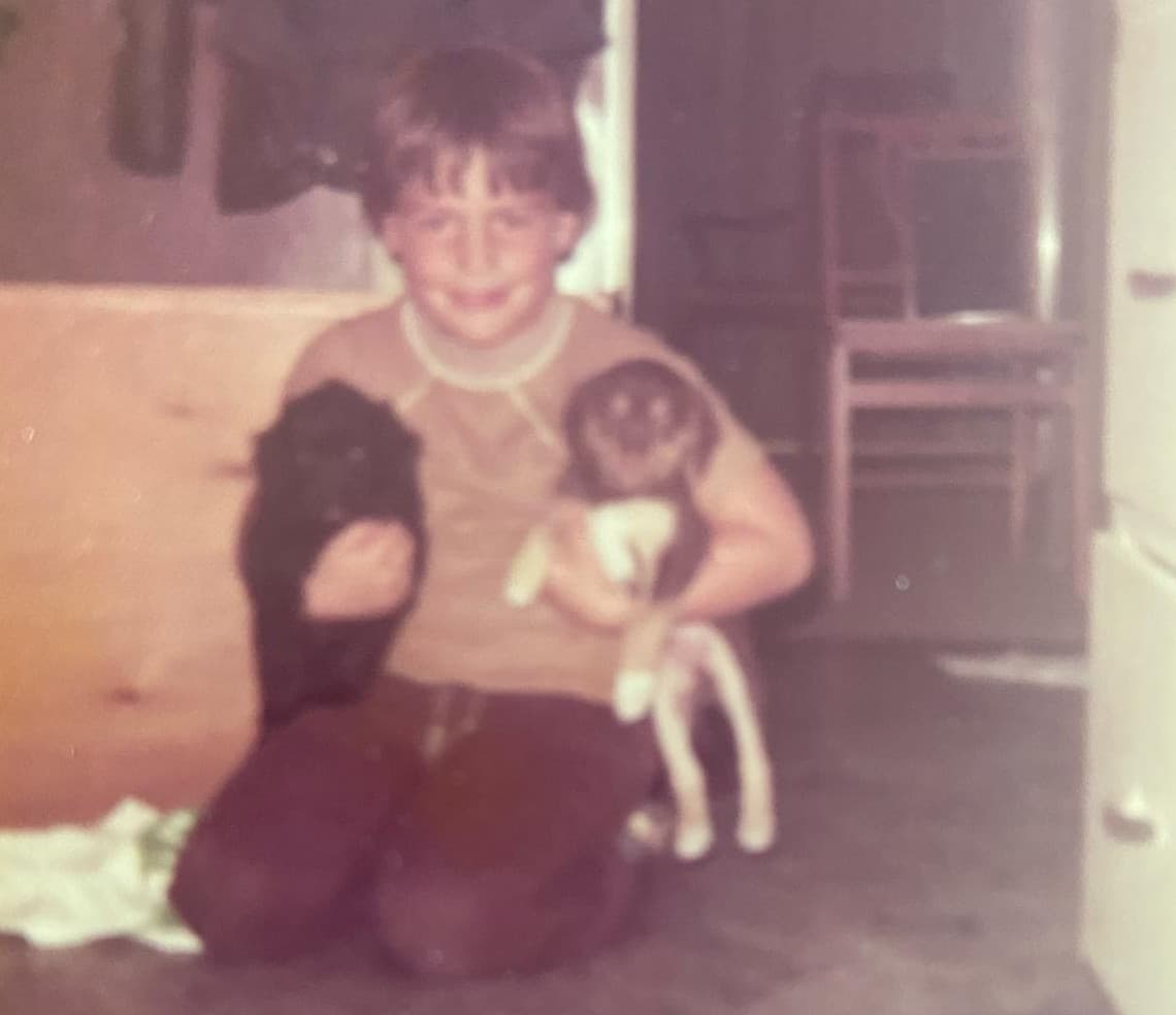 Michael Scarano as a young boy, kneeling on the floor holding two puppies