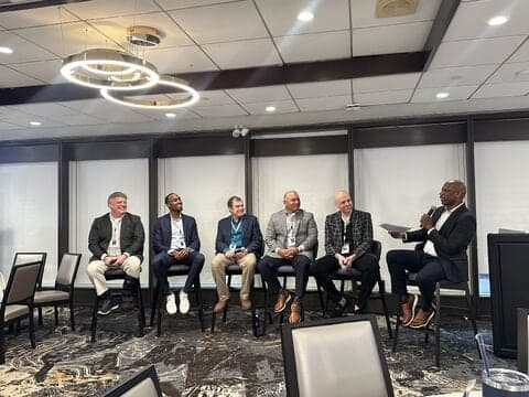 A panel of speakers seated on stage at a corporate event